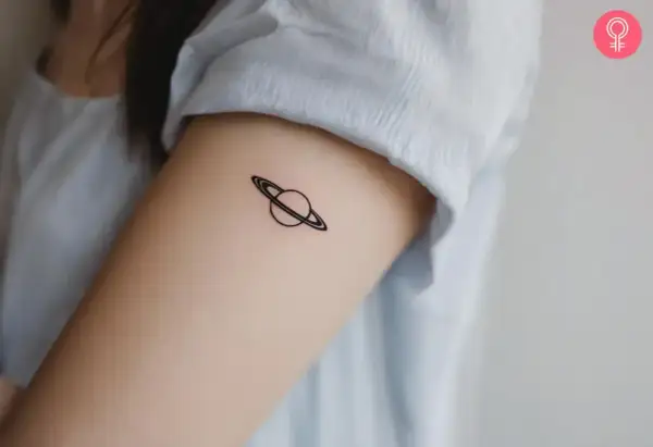 Tatuaje minimalista de Saturno en el brazo. Tatuarse Saturno puede simbolizar madurez, responsabilidad y el paso del tiempo.