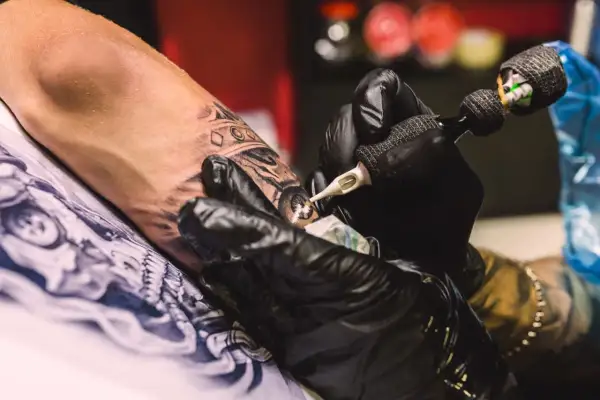 Manos enguantadas crean arte en la piel, un detalle de la **convención tatuajes**.