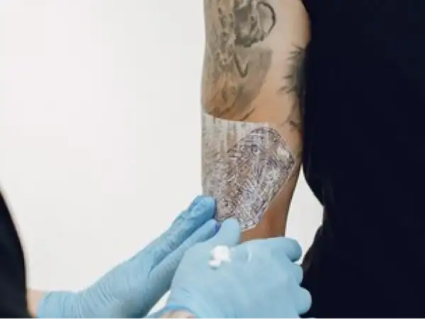 Manos enguantadas aplican Bepanthol sobre un tatuaje para ayudar a su curación.