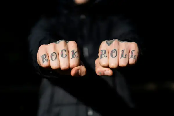 Manos con tatuajes en los nudillos que dicen "ROCK ROLL". A pesar de la pena y el pánico, el rock and roll vive.
