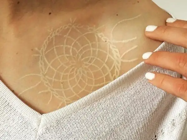 Un delicado tatuaje white out con diseño de atrapasueños en la clavícula.