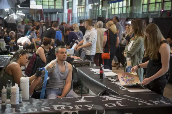 En la convencion tattoo barcelona, un artista tatúa un brazo mientras otros observan diseños.