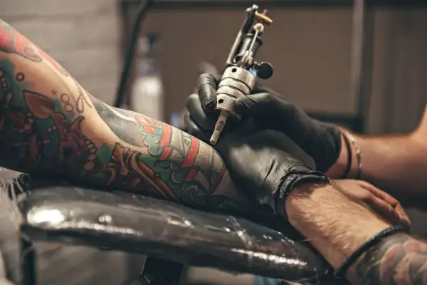 Primer plano de un brazo con tatuajes coloridos siendo tatuado por una máquina.