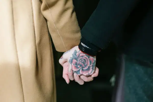 Manos entrelazadas, una con un tatuaje de rosa roja, mostrando el arte de los tatouages homme.