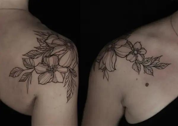 Delicados blackwork tattoos de flores y hojas adornan los hombros, creando un diseño botánico elegante y atemporal.