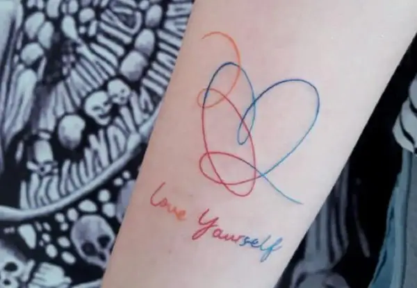 Tatuajes de corazón y "Love Yourself" en el brazo, un símbolo de fortaleza y amor propio.