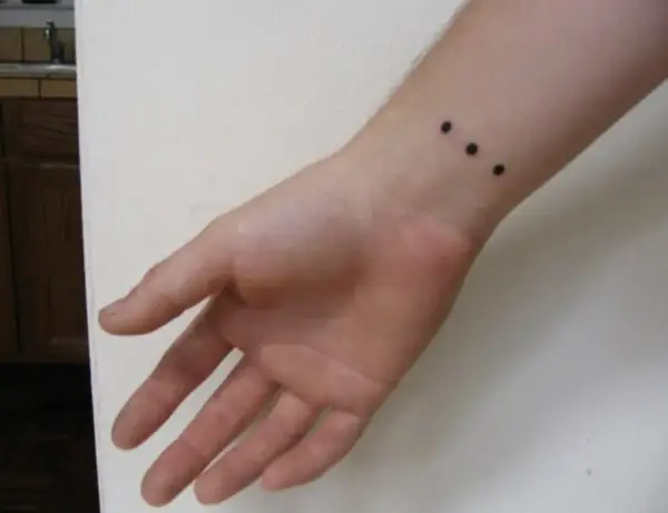 Muñeca con un discreto tatuaje de tres puntos negros alineados.