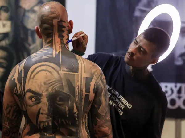 Artista de **val tattoo** retocando un intrincado diseño en la nuca de un hombre.