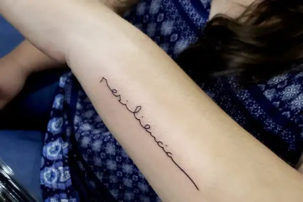 Tatuaje de "resiliencia" en el brazo, un símbolo de la fuerza de la mujer.