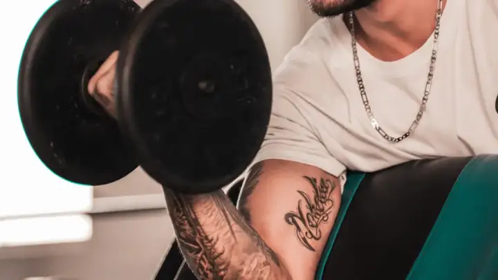 Hombre con tatuaje levanta pesa, mostrando su dedicación al deporte y su arte corporal.